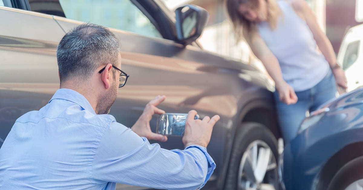 man taking picture on phone after car accident